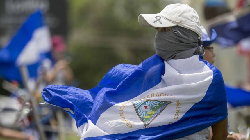 Una joven con la cara tapada y la bandera de Nicaragua