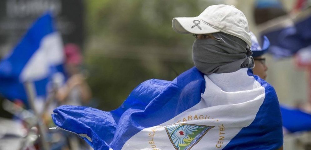 Una joven con la cara tapada y la bandera de Nicaragua